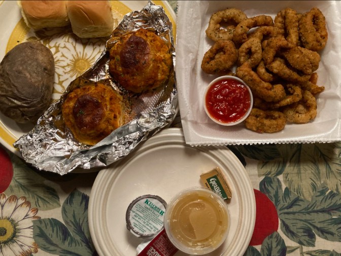 Table with fried calamari, crabcakes, potato, rolls, and applesauce.