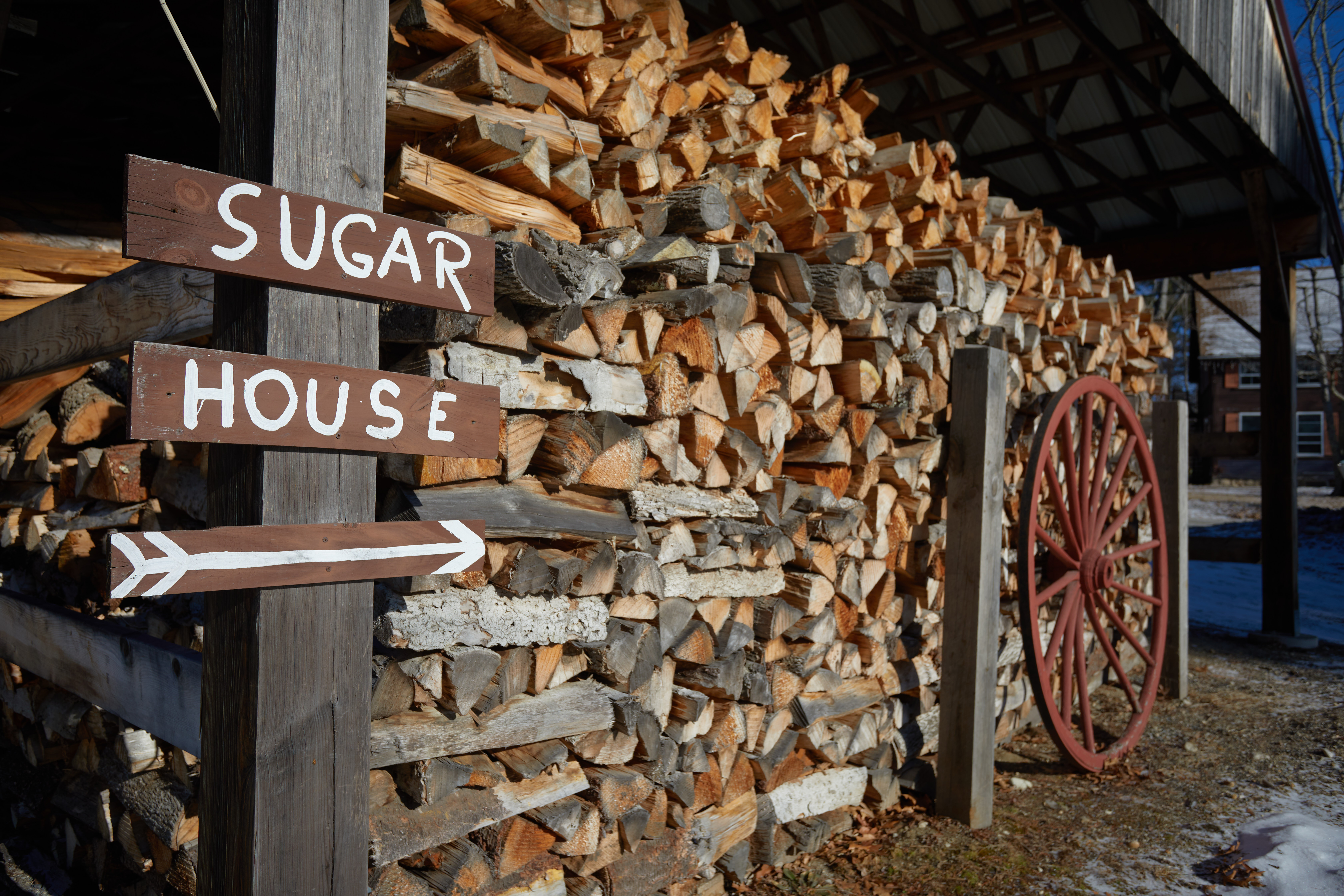 Wood pile with wooden sign beside it that reads SUGAR HOUSE.
