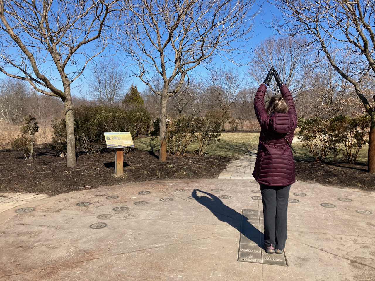 Woman standing with arms raised on sundial.