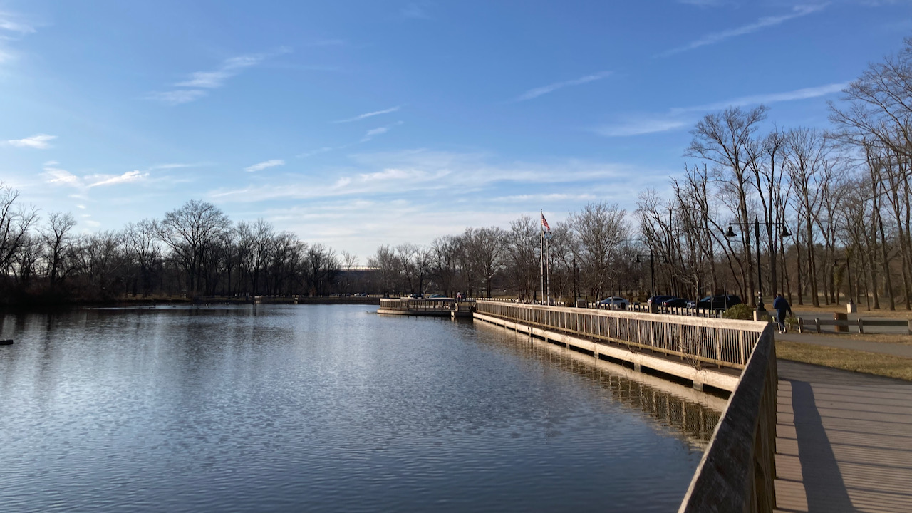 Boardwalk path beside small pond in park.
