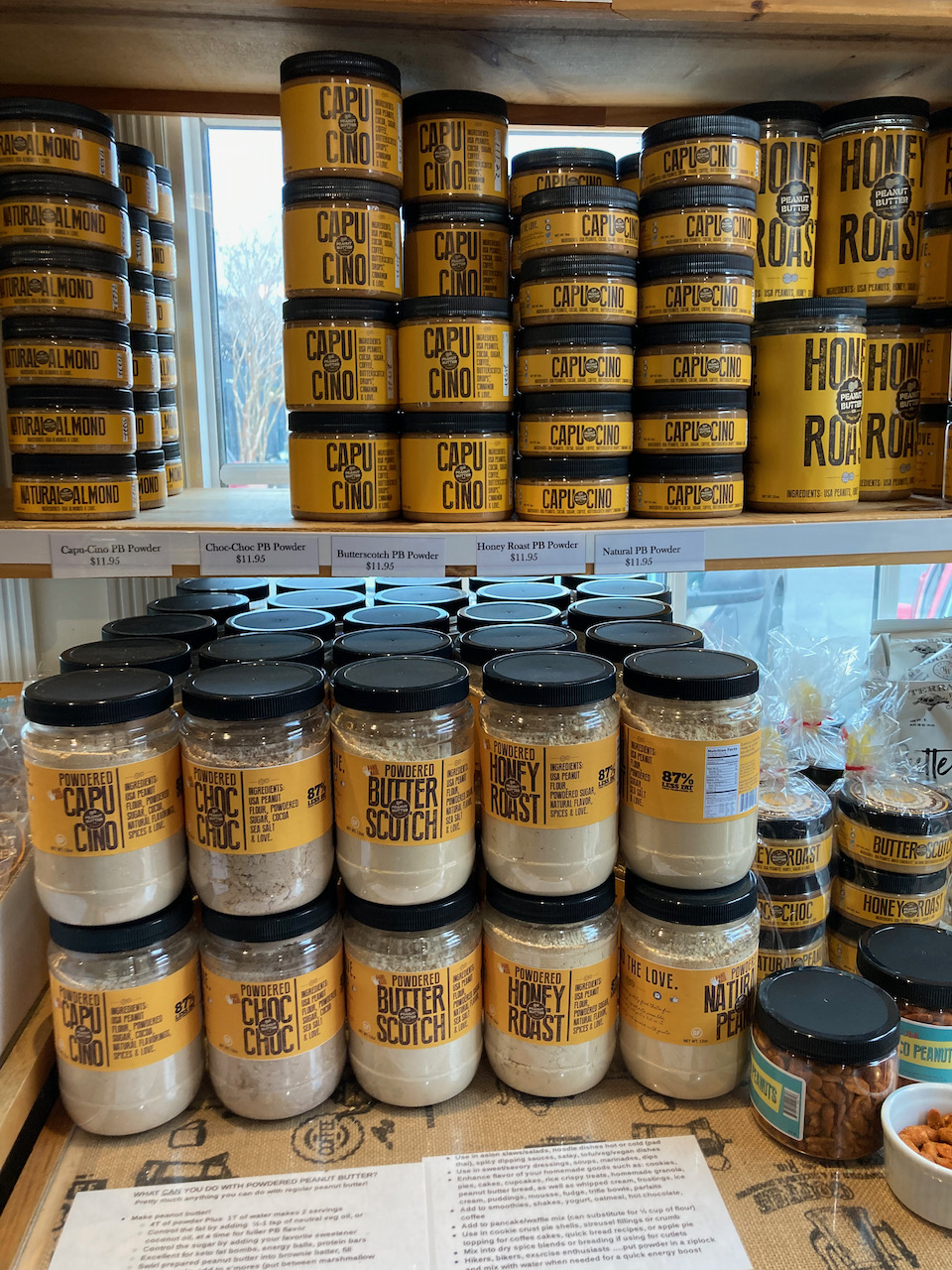 Varieties of peanut butter on shelves in plastic containers.