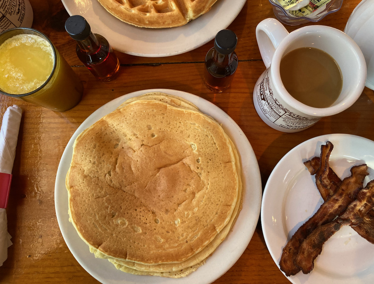 Pancake on plate, bacon on plate, cup of coffee, and glass of orange juice.