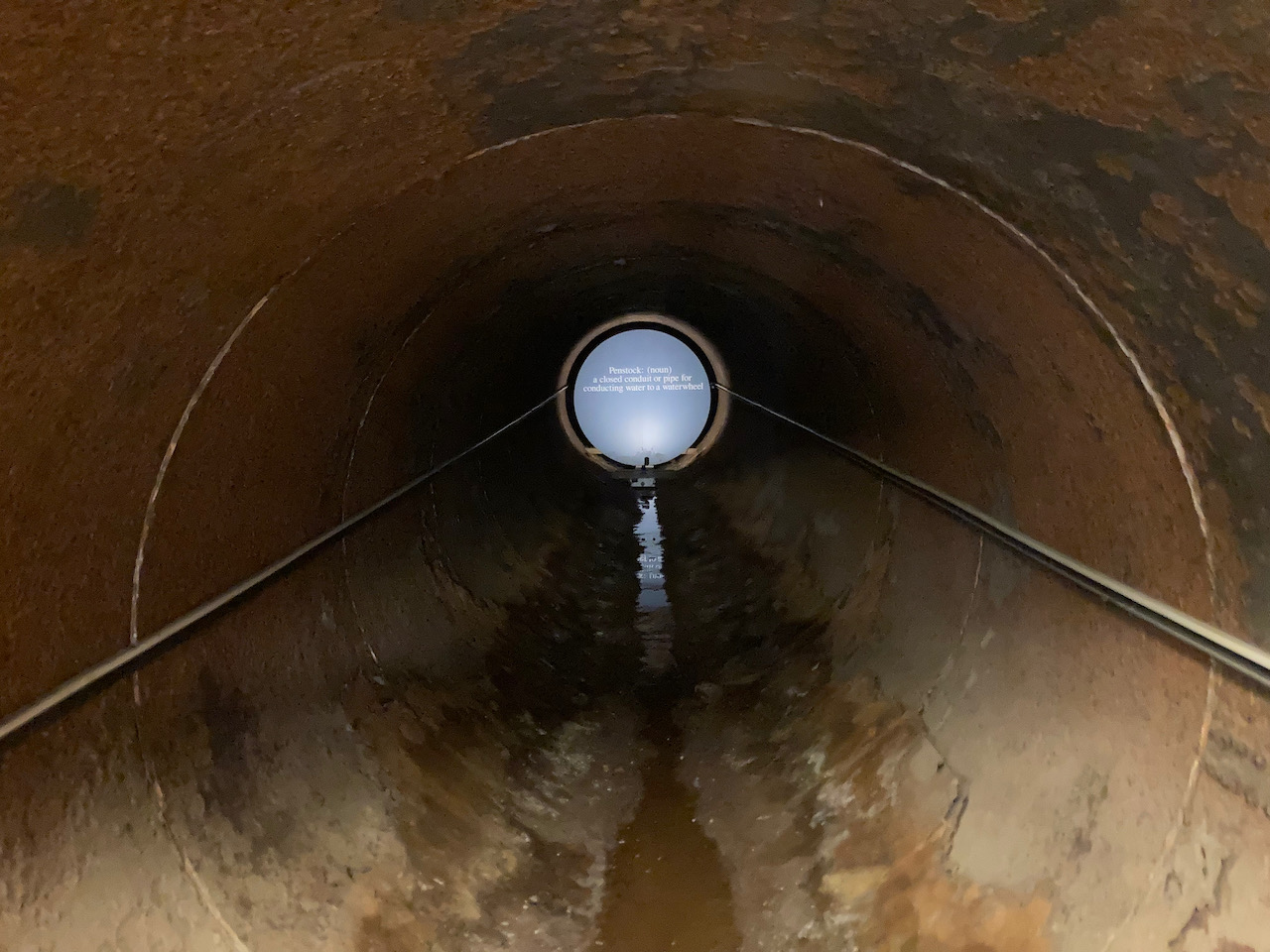 Inside of large steel tunnel, with lighted sign at end.