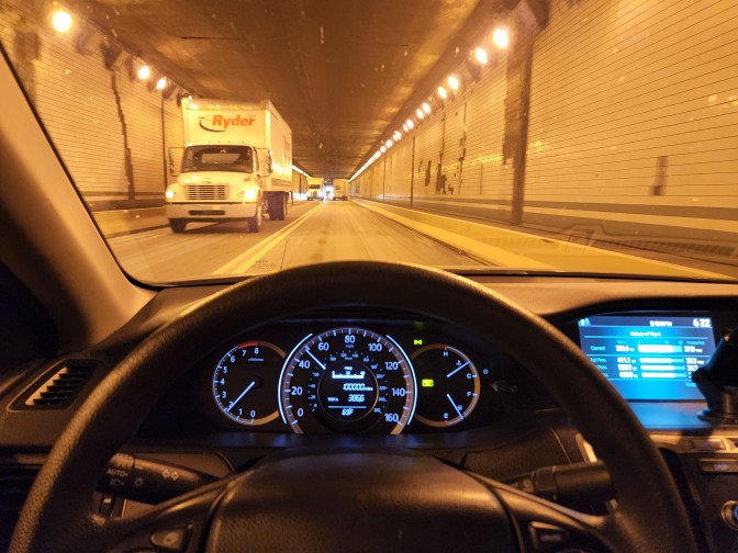 View of tunnel through front window of Honda Accord. Odometer in dashboard reads 100000 miles.