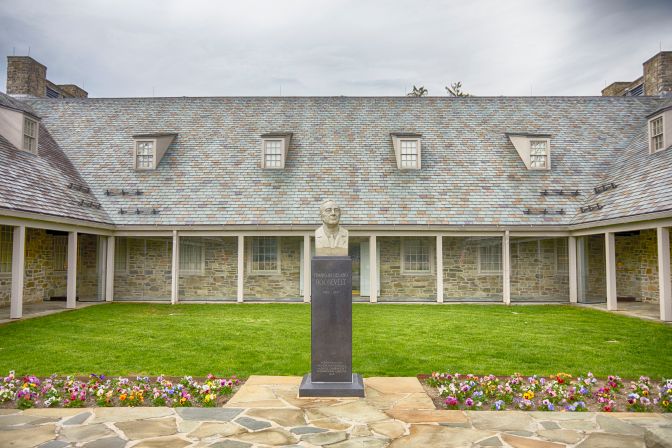 Exterior of Franklin D. Roosevelt Library and Museum, with a bust of FDR on pedestal in foreground in front of courtyard.