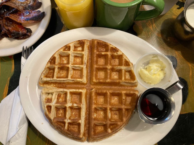 White plate with belgian waffle, butter, and syrup.