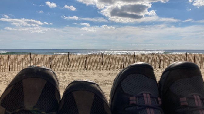 Toes of shoes in foreground, with beach and waves in background.