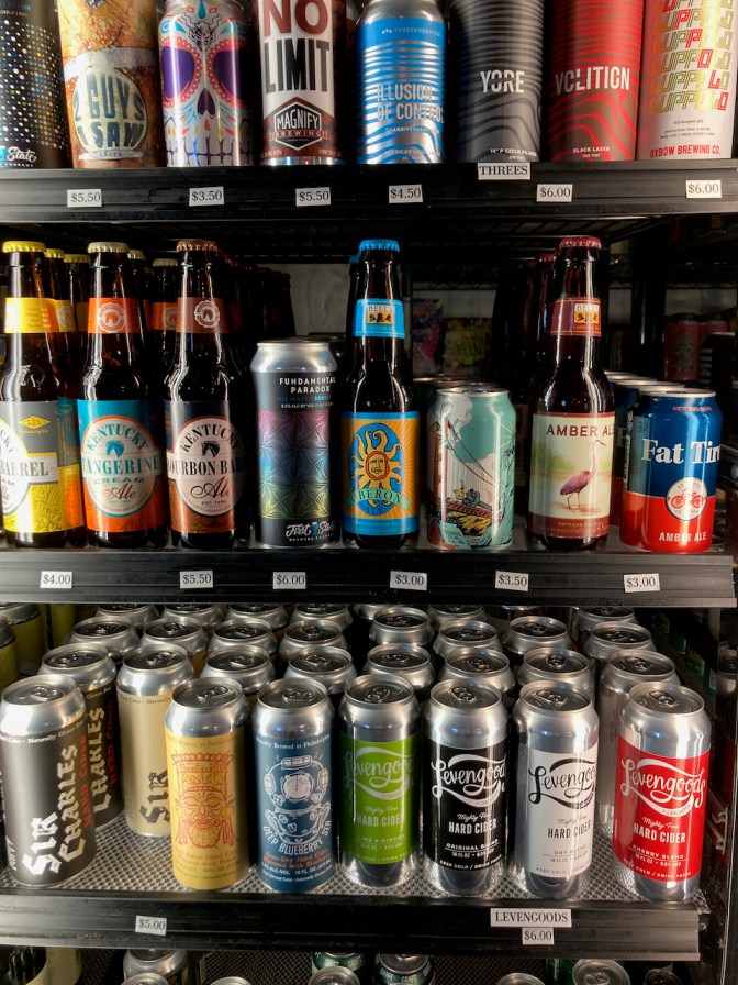 Beer cooler filled with various craft beers in cans and bottles.