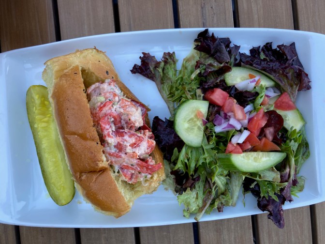 Plate with lobster roll, pickle, and salad.
