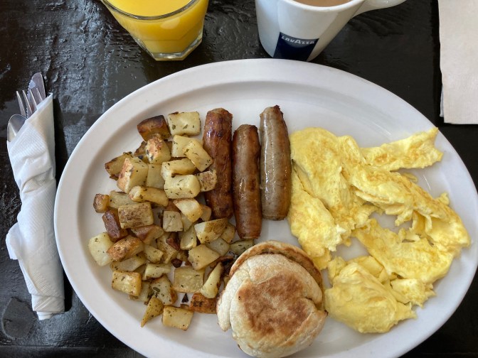 Scrambled eggs, sausage, home fries, and English muffin on plate.