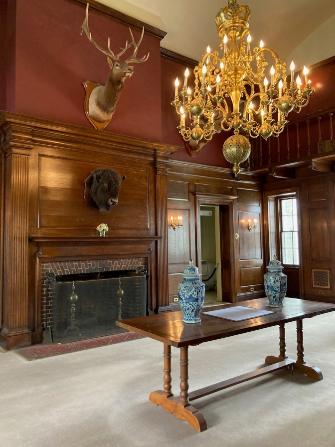 Interior hallway of pavilion, with chandelier hanging from ceiling and mounted animals heads on wall above fireplace.