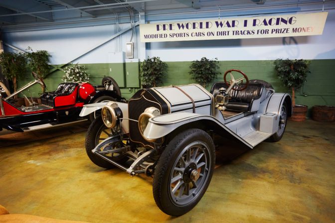 1912 National Model 40 in front of sign that says PRE WORLD WAR I RACING Modified Sports Cars on Dirt Tracks for Prize Money.