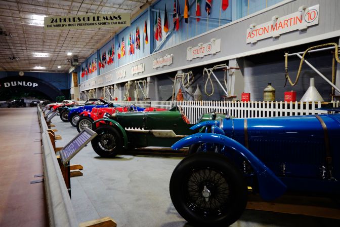 Recreation of pit lane from Le Mans, with several race cars in pits. A sign hangs from ceiling that says 24 HOURS OF LE MANS.