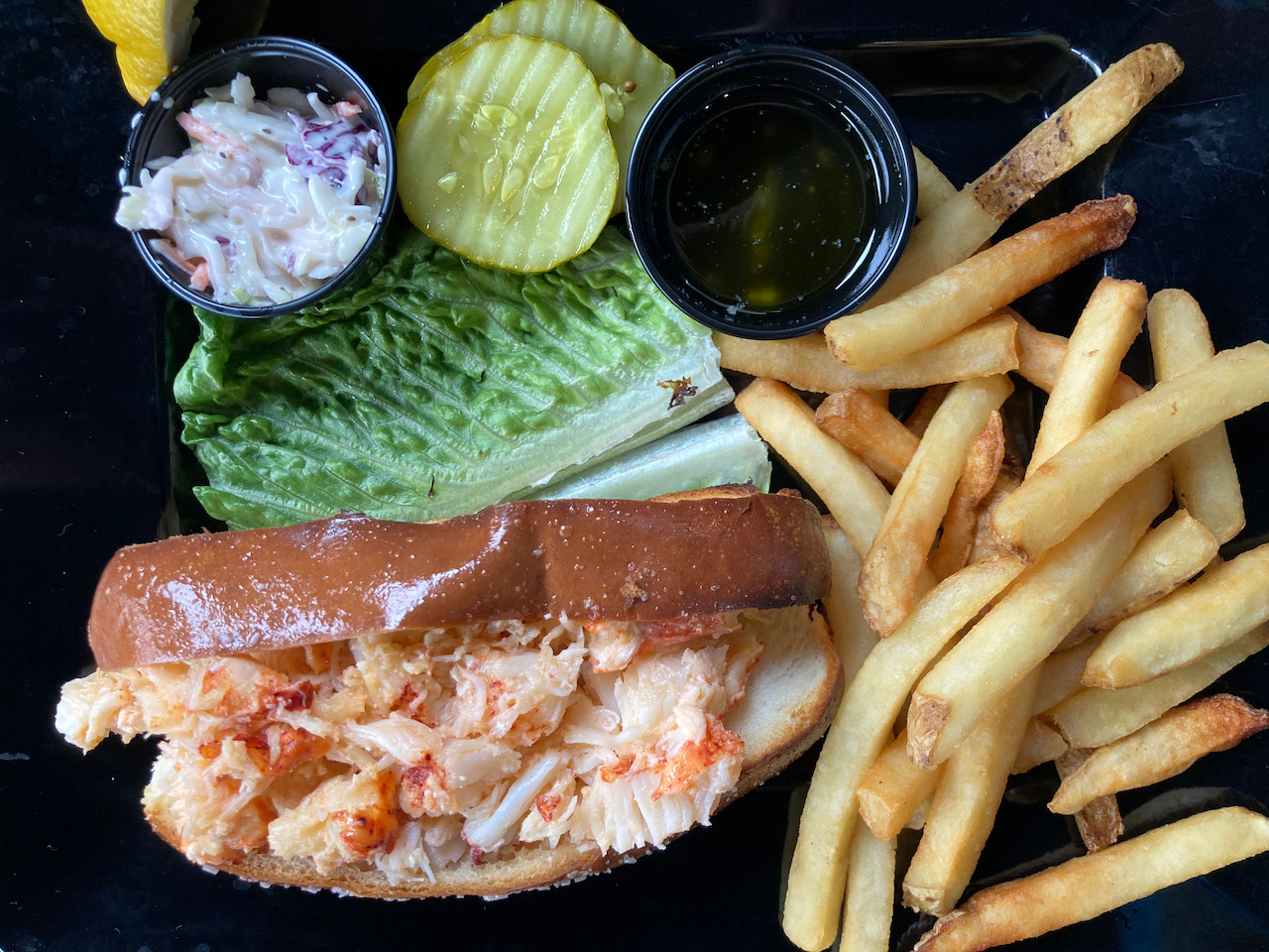 Lobster roll, french fries, pickles, and coleslaw on plate.