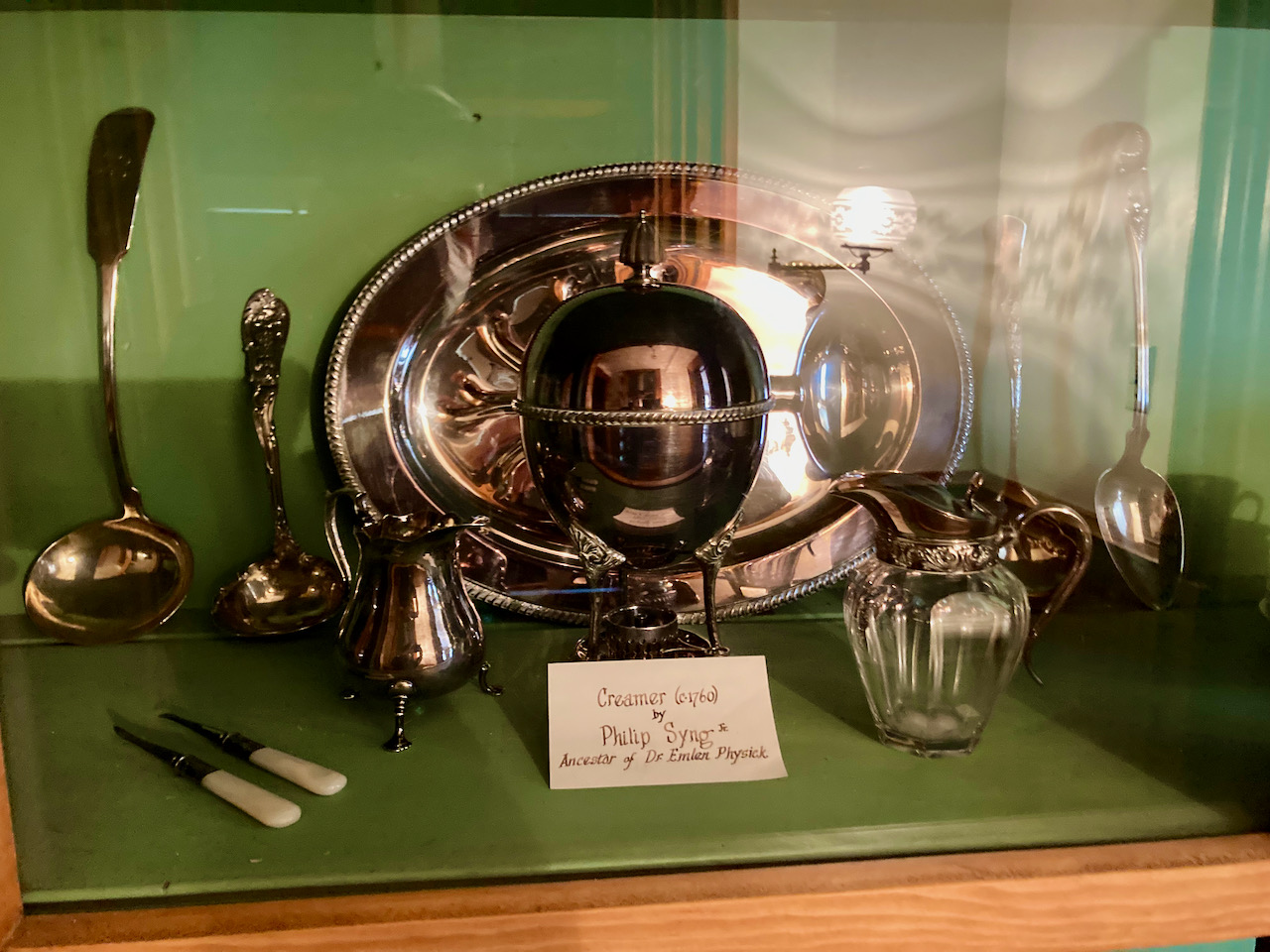 Collection of silverware and other serving items in glass cabinet.