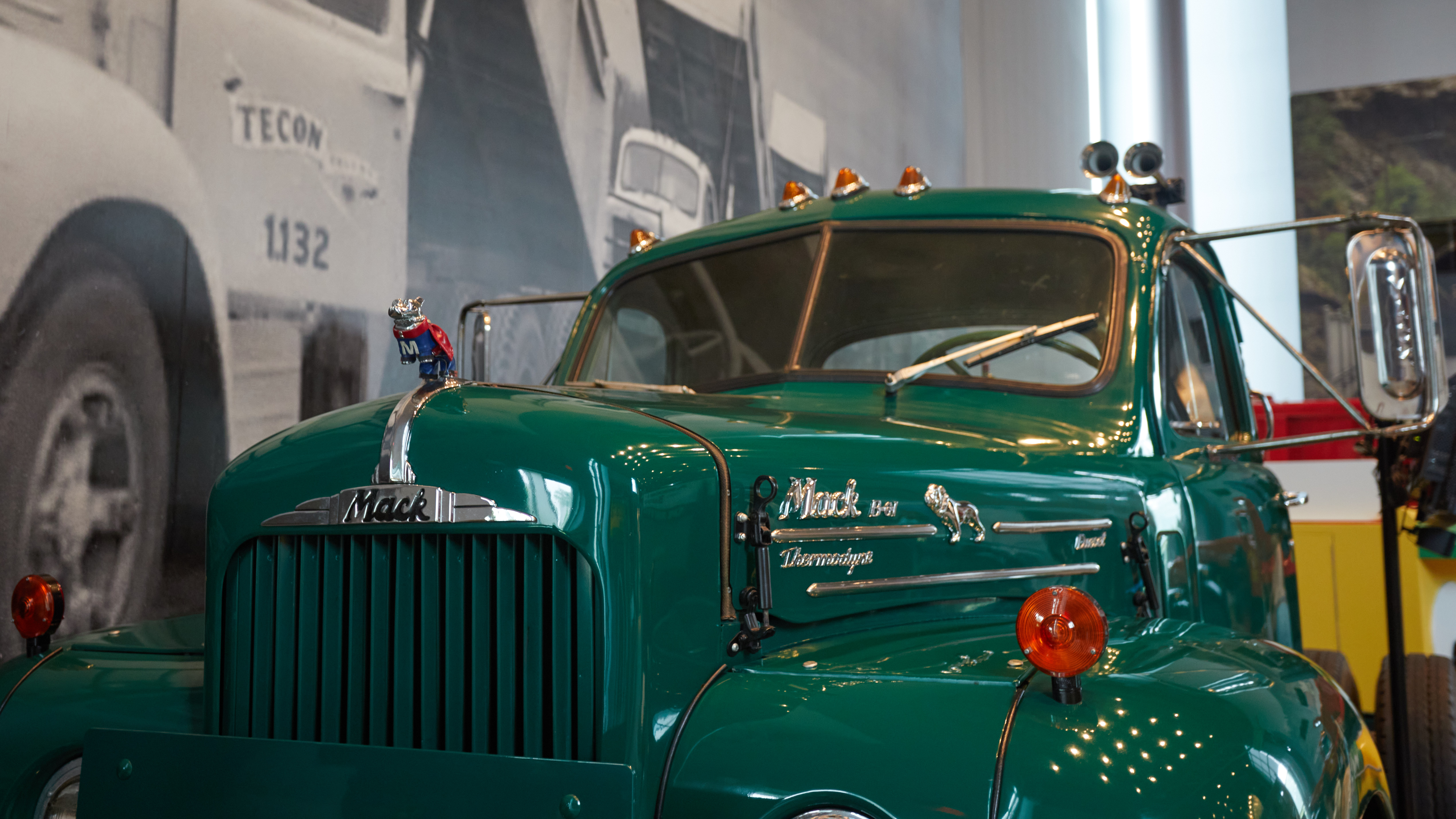 Front of green Mack truck, with focus point on bulldog emblem on hood.