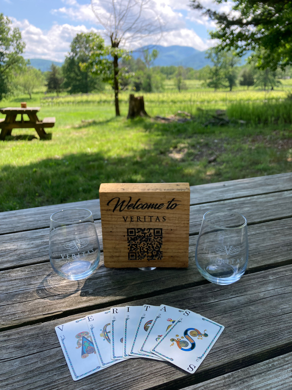 Picnic table with playing cards, two glasses, and a wooden sign that says WELCOME TO VERITAS.