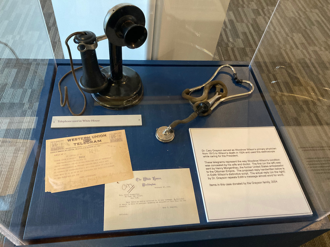 Telephone, stethoscope, and telegram on display in glass case.