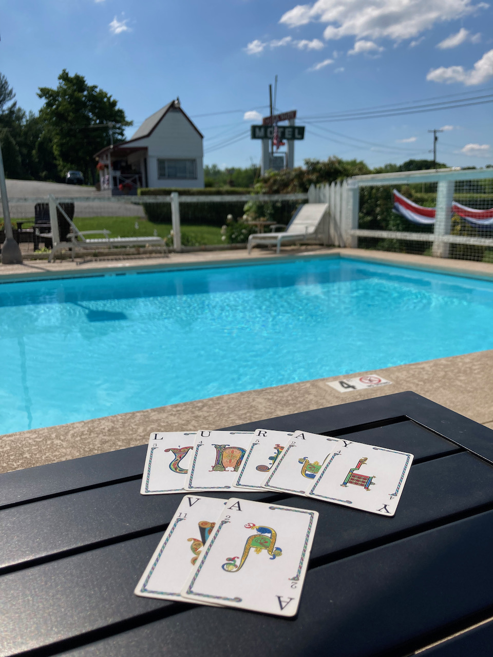 Swimming pool, with playing cards on picnic table in foreground.