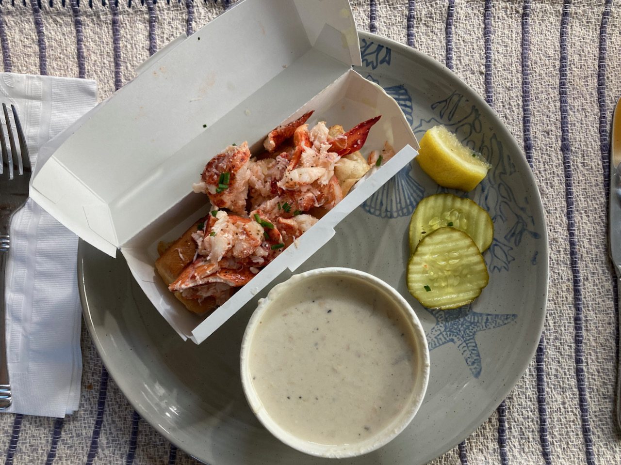 Lobster roll and cup of New England Clam Chowder on plate.