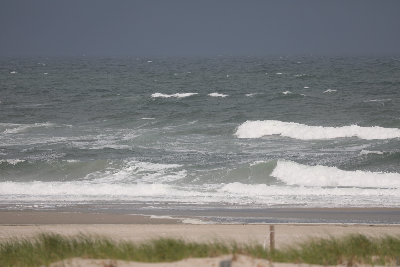 Rough seas and gray sky, with beach in foreground.