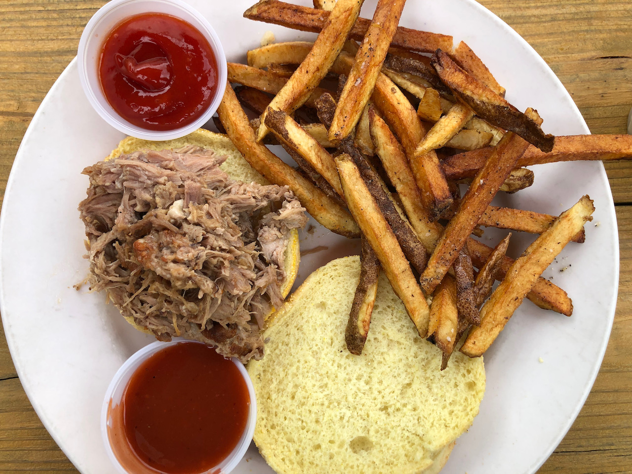 Pulled pork sandwich on white plate, with french fries.