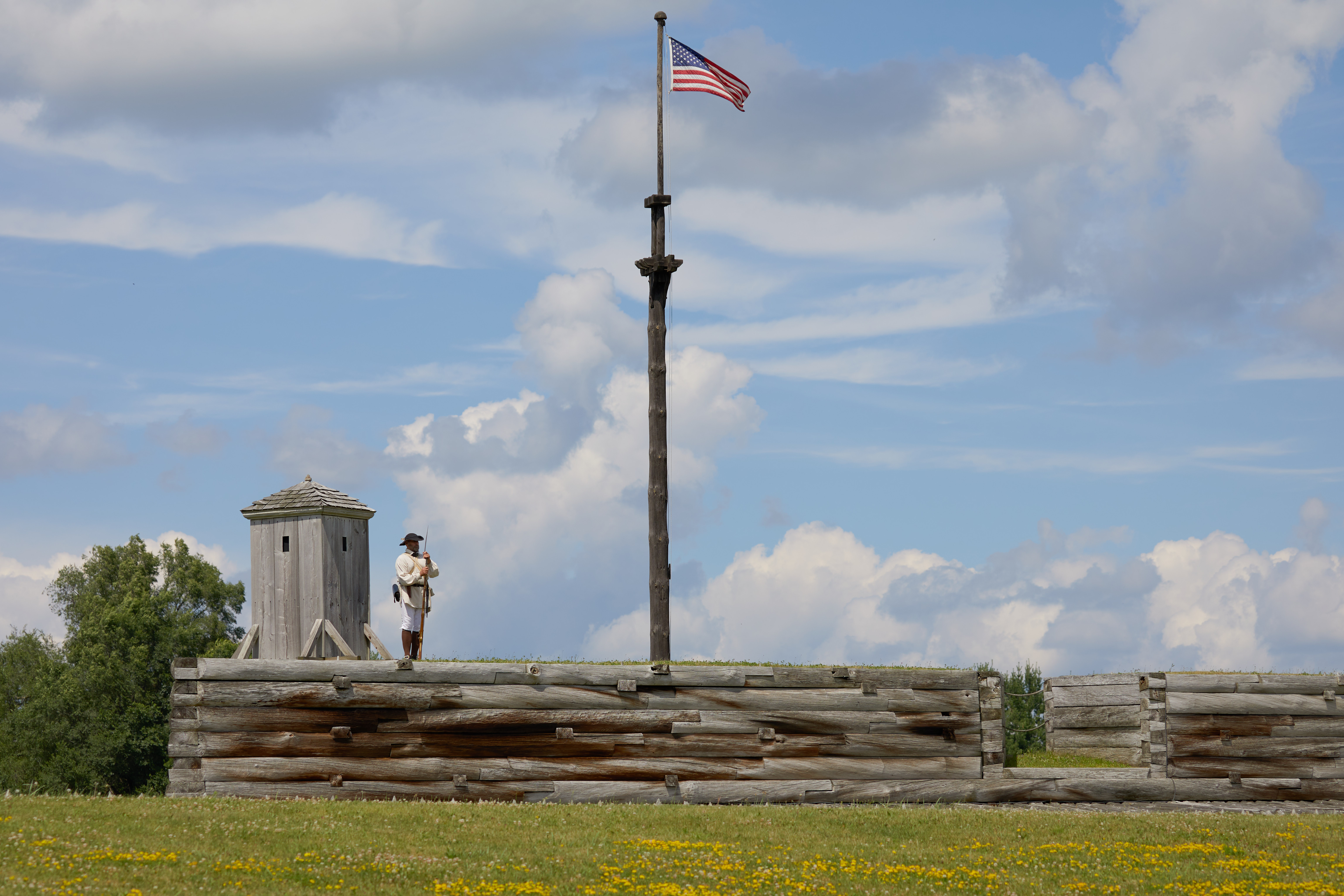 Soldier standing on rampart of Fort Stanwix, with American flag flying on pole.