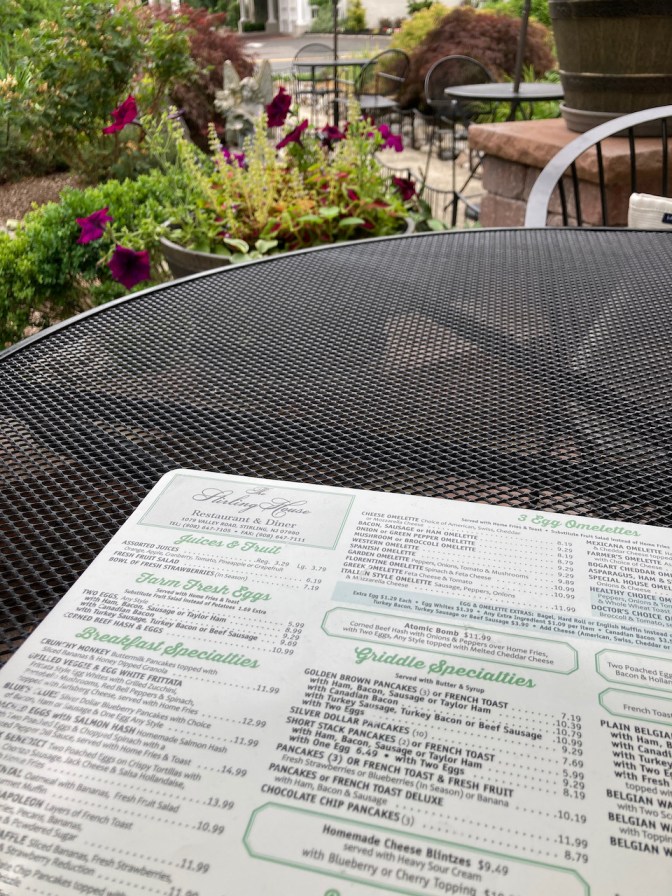 Menu of The Sterling House on metal picnic table, with garden in background.