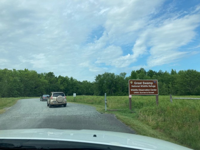Entrance to Great Swamp National Wildlife Refuge, with two cars in gravel driveway.