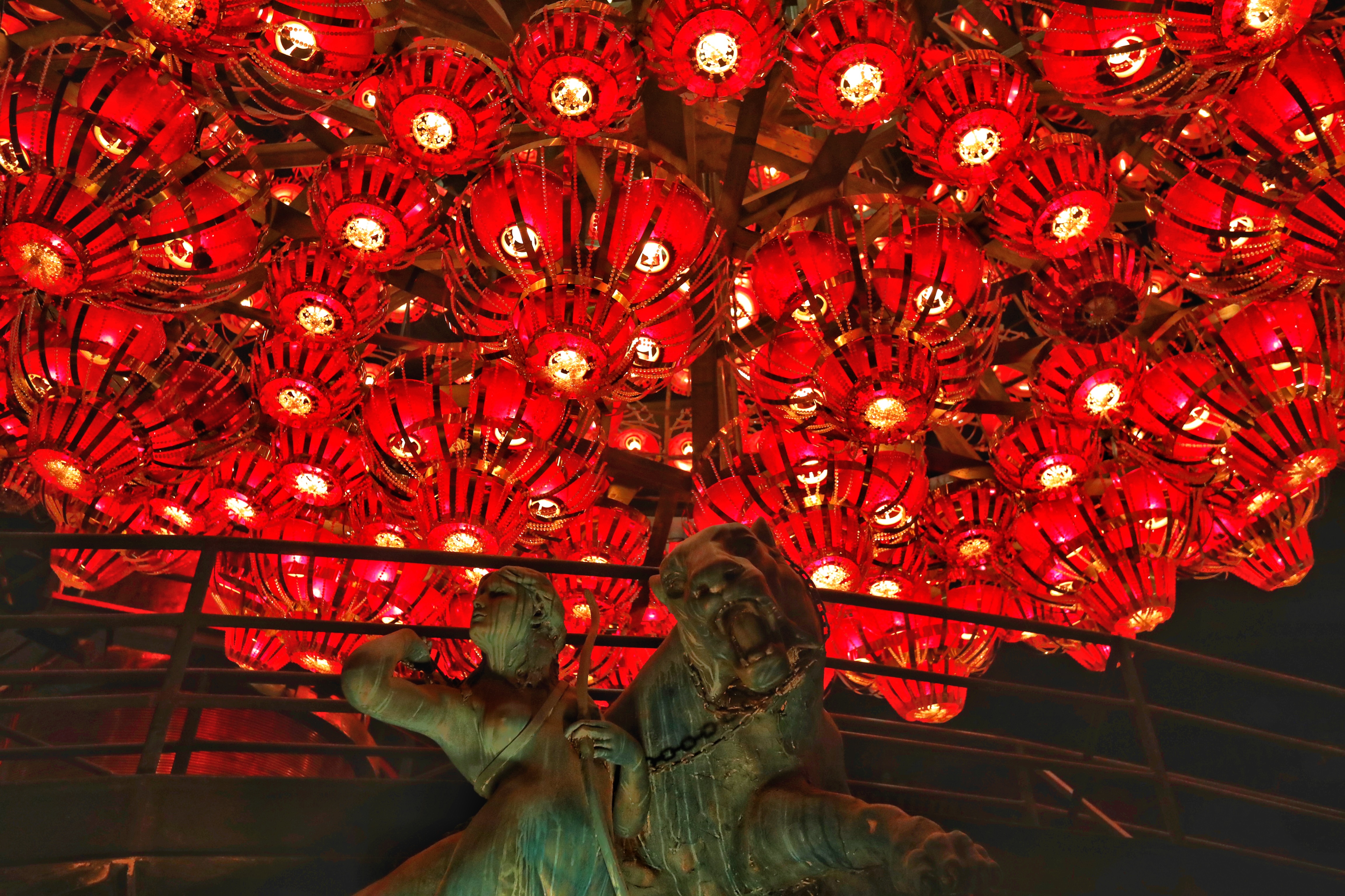Statue of woman and lion, with red chandeliers above.