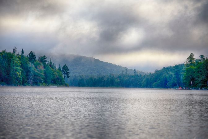 View of lake, with clouds over mountains in distance.
