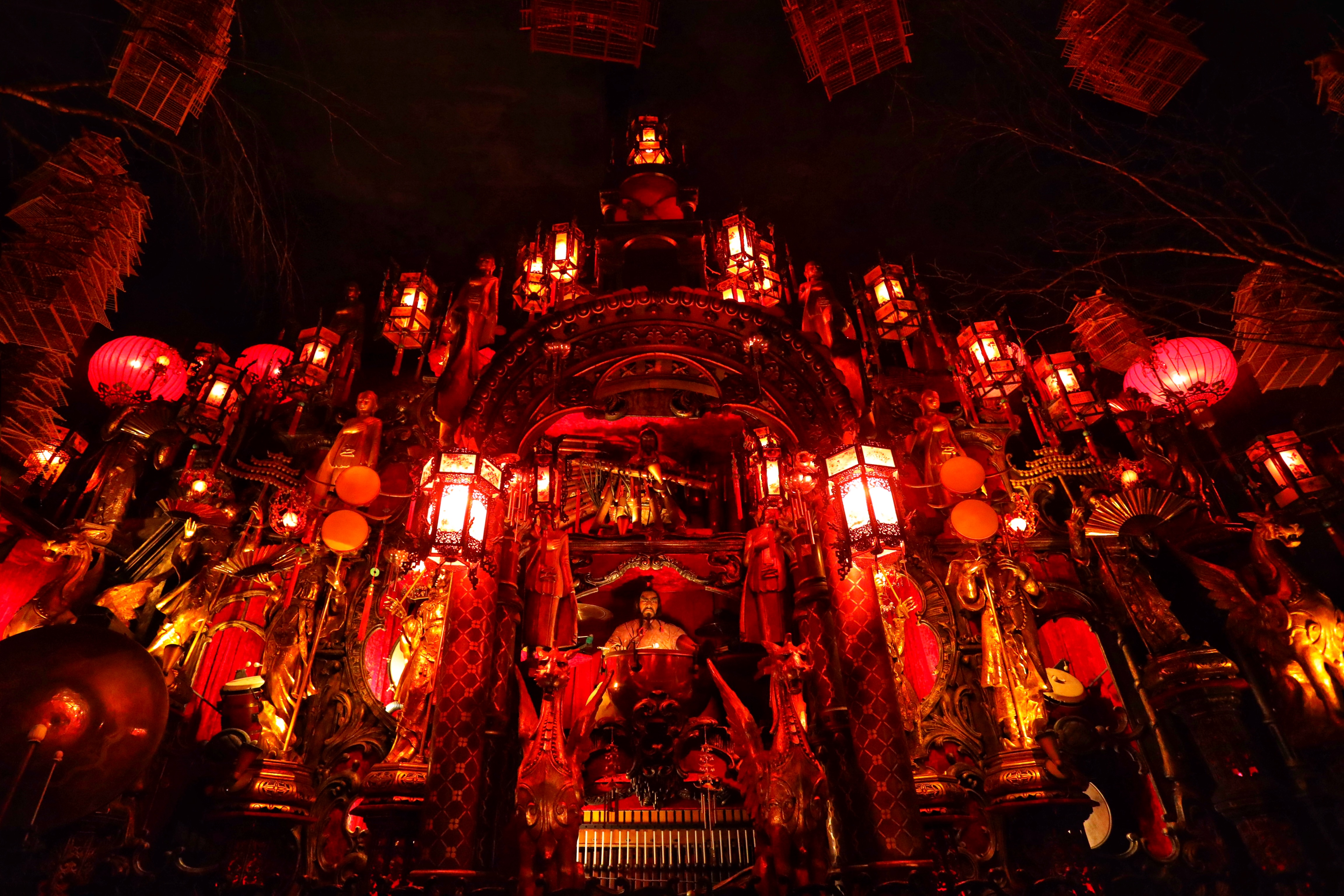 Room with red light, illuminating Chinese lanterns, statues, and musical instruments.