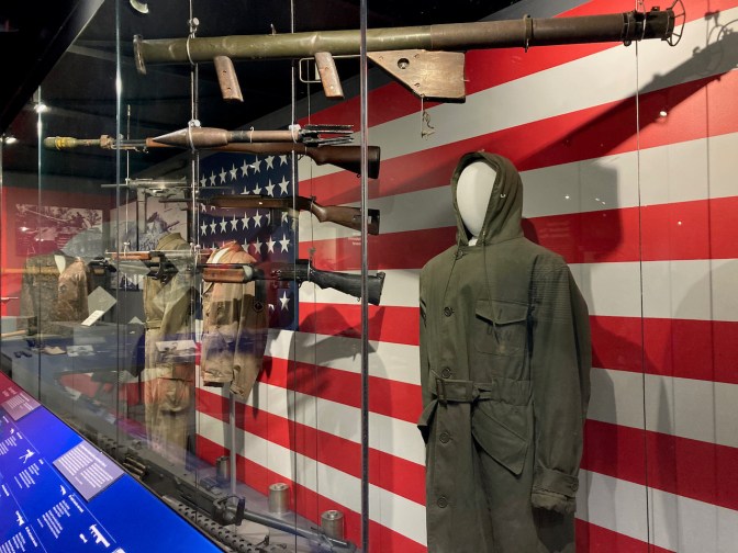 Mannequins with uniforms and guns, in front of an American flag.