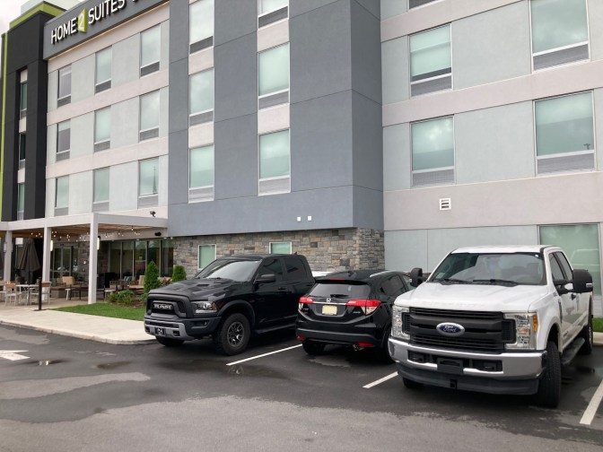 2021 Honda HR-V parked between two pickup trucks in front of hotel.