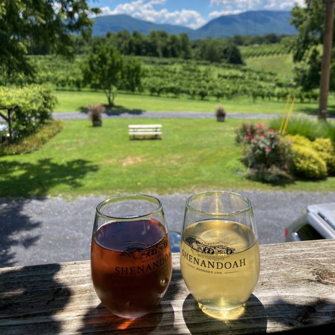 Two glasses of wine, placed on porch bannister overlooking vineyard.