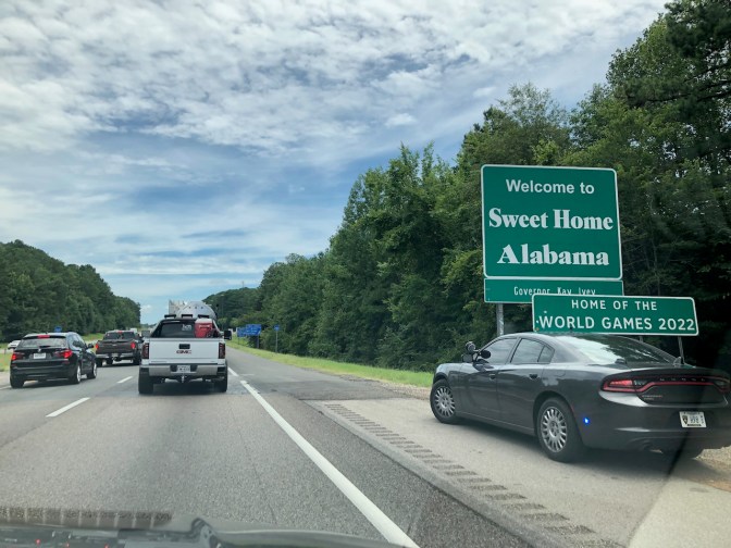 Interstate highway filled with traffic. Sign on side of road says WELCOME TO SWEET HOME ALABAMA.