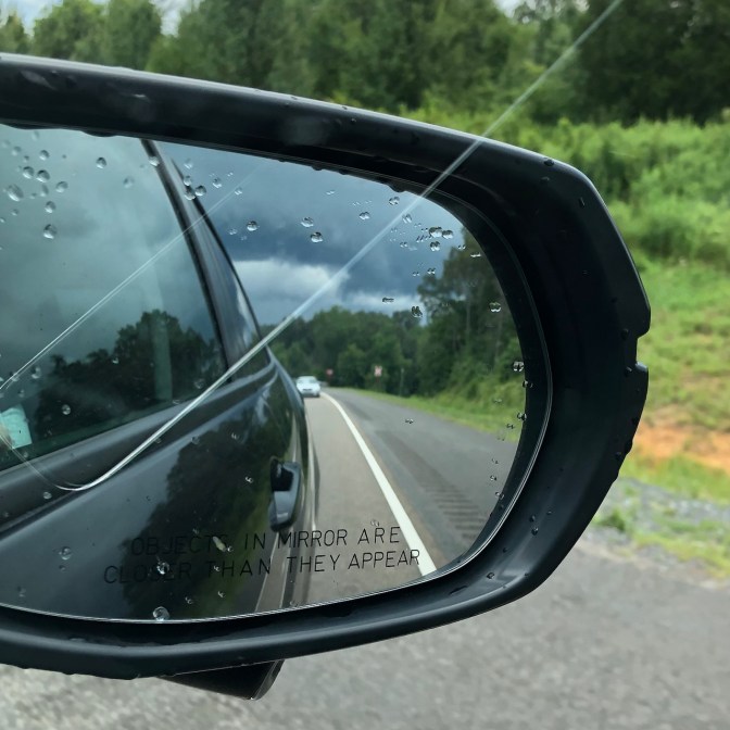 Rearview mirror of car, with rain clouds in sky in mirror image.