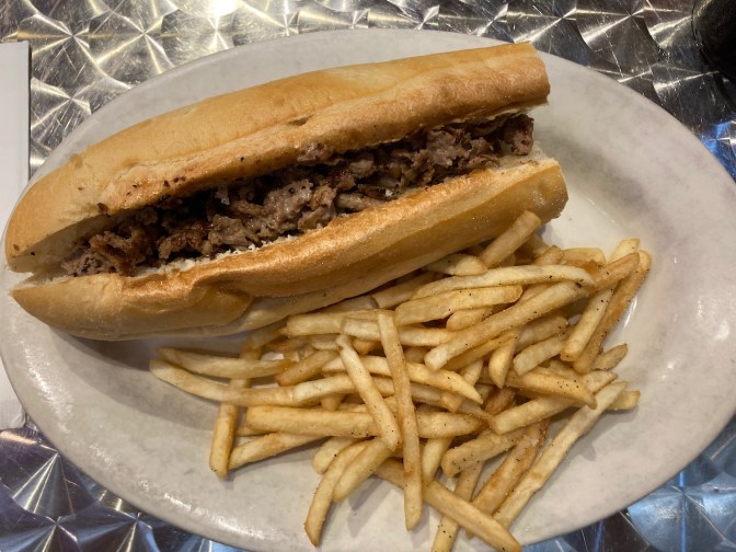 Cheesesteak and french fries on plate.