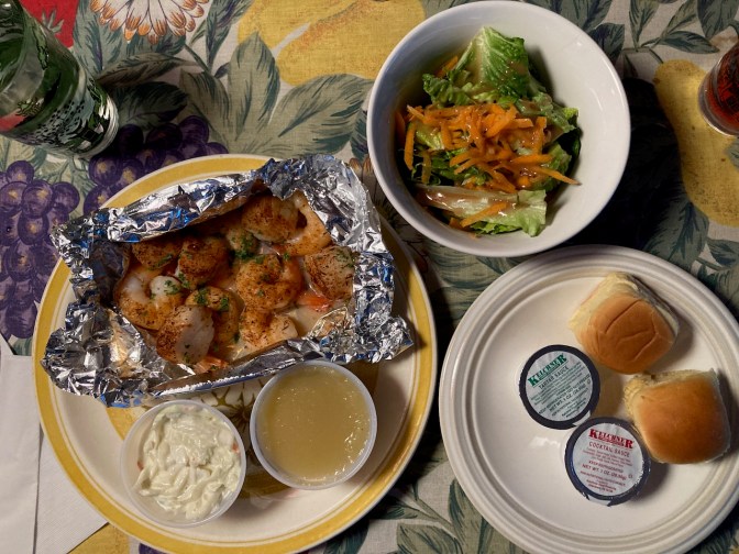 Plate with grilled shrimp and scallops, a bowl with a salad, and a plate with rolls, on a table.