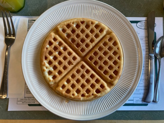 Waffle on plate, with knife and spoon on one side of placemat, and fork on the other.