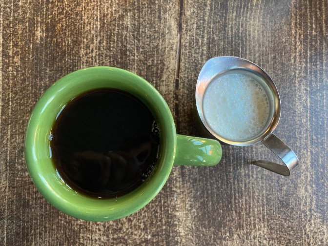 Coffee in cup, with cream in small steel pitcher.