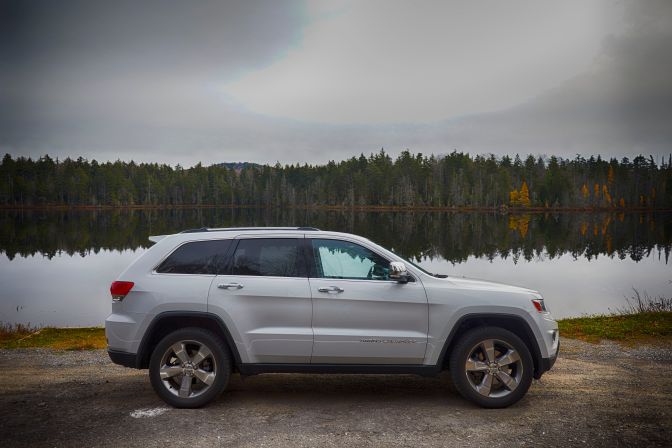 2014 Jeep Grand Cherokee parked beside tree-lined pond.