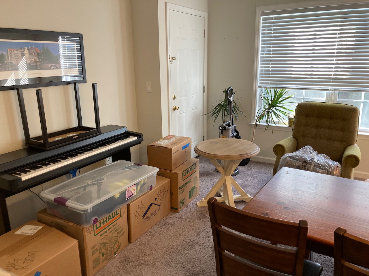 Apartment filled with boxes, electric piano, tables, and chairs.