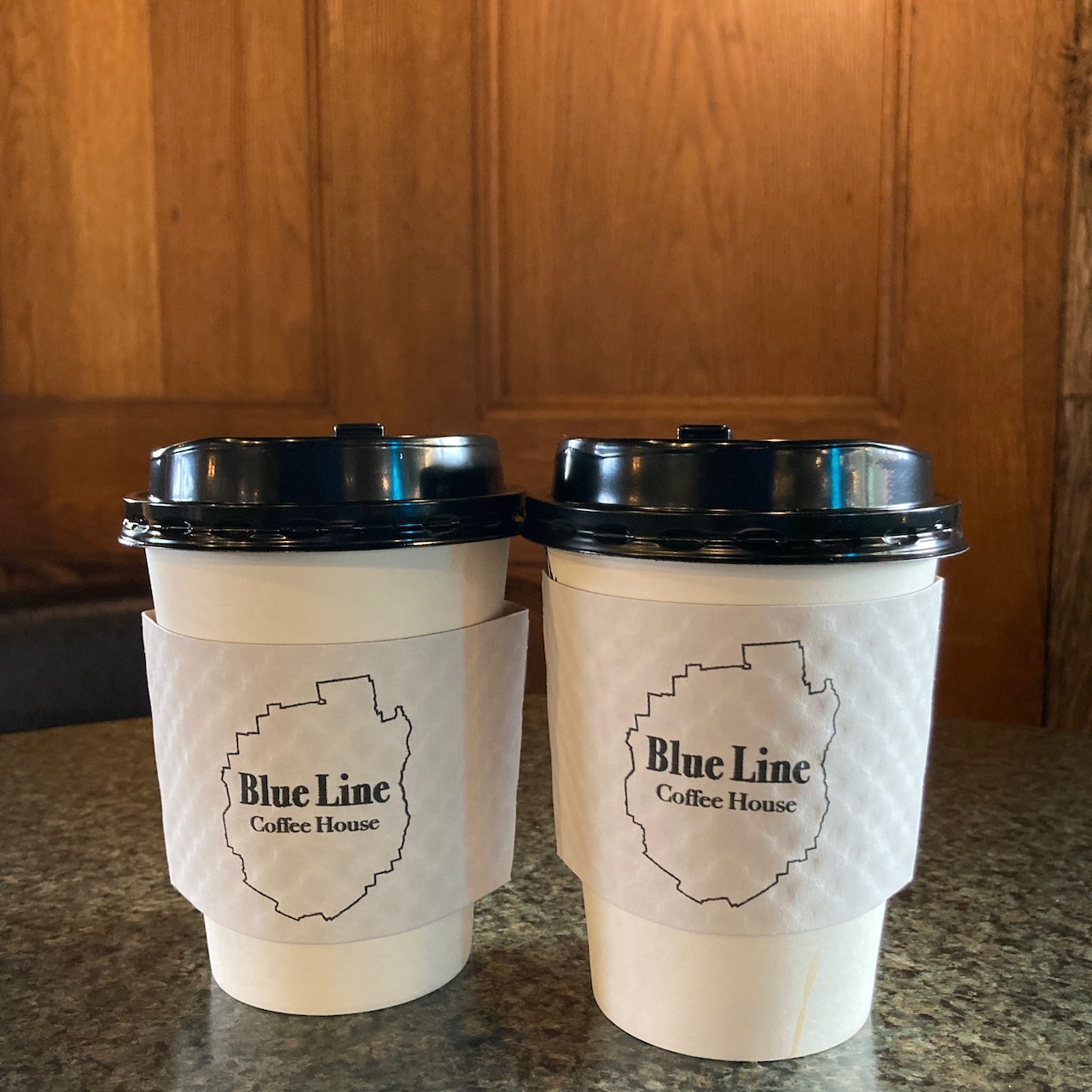 Two cups of coffee on marble table. Both cups say Blue Line Coffee House.