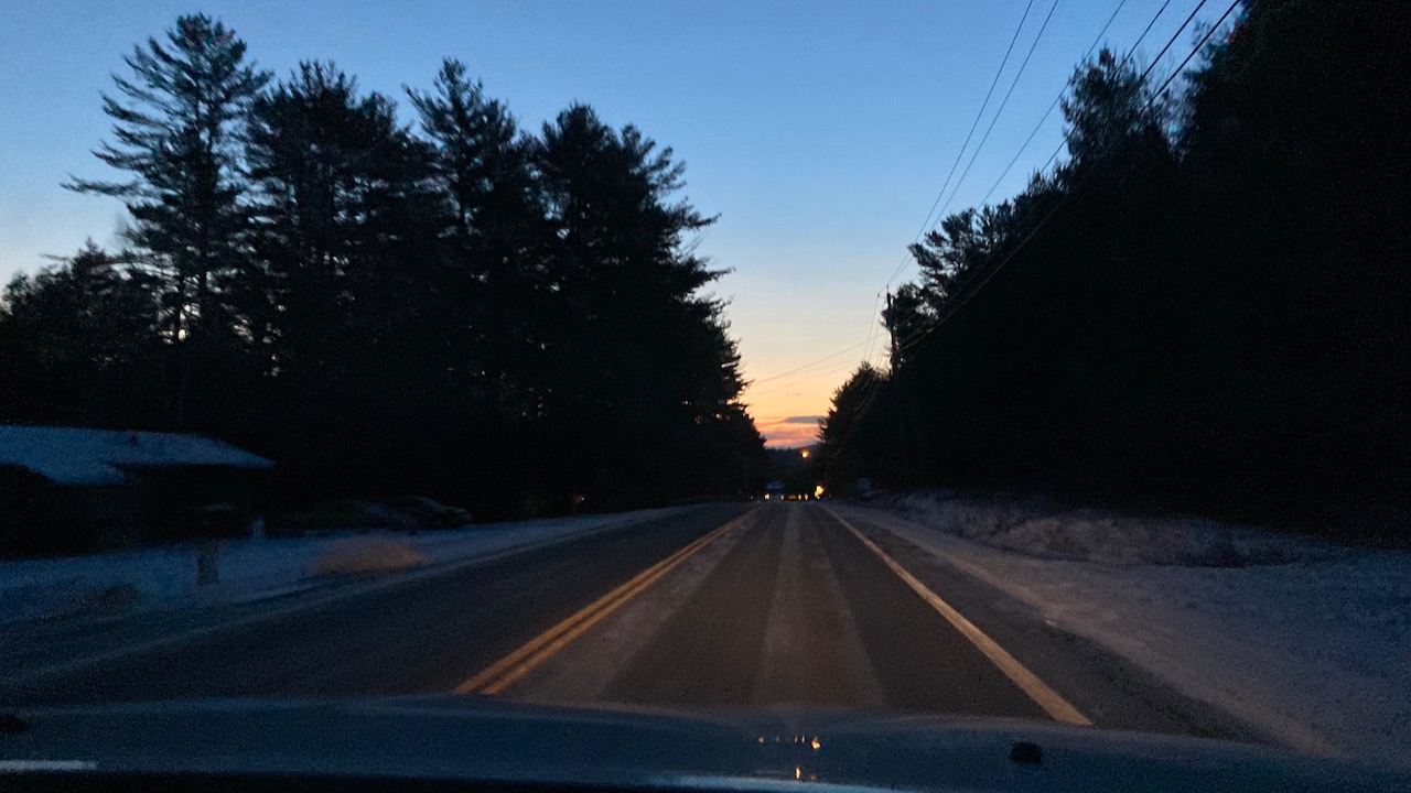 View of two-lane road with sunrise in distance.