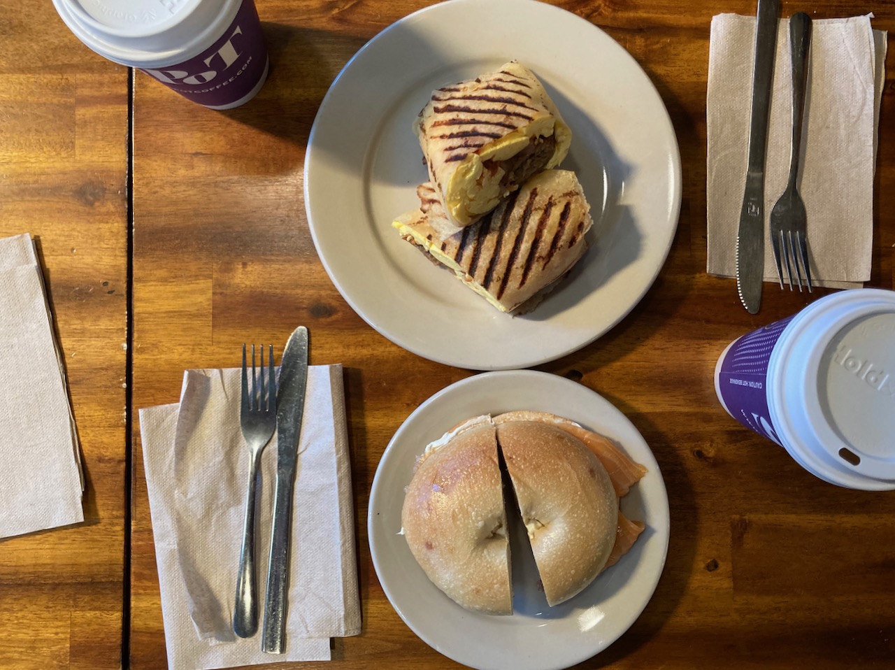 Breakfast wrap on plate and bagel sandwich on plate, both on wooden table.