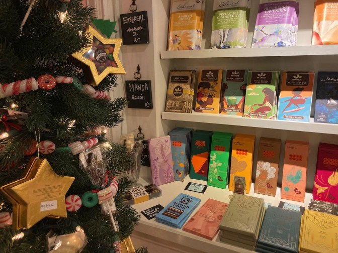 Bars of chocolate on display on shelves. A Christmas tree is in the foreground.