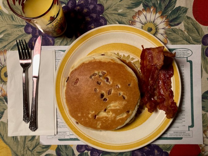 Pancakes and bacon on plate, with glass of orange juice beside plate.