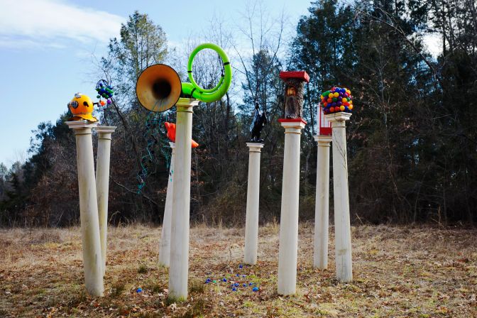 Modern art sculpture of art set atop pillars in wooded clearing.