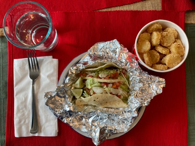 Tacos, potato oles, and glass of water on table.
